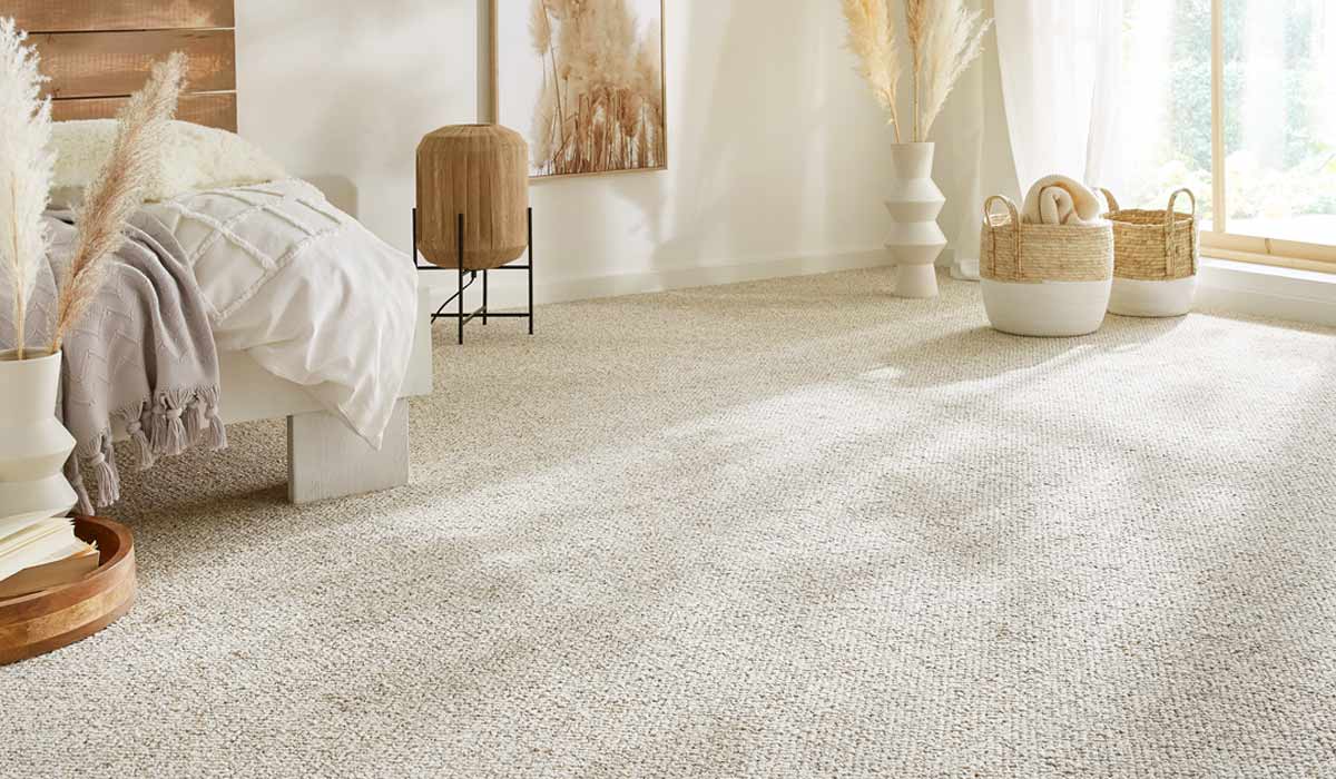 Schlafzimmerbett steht auf hellem Teppichboden, umgeben von Körben, Vasen und trockenen Pflanzen.