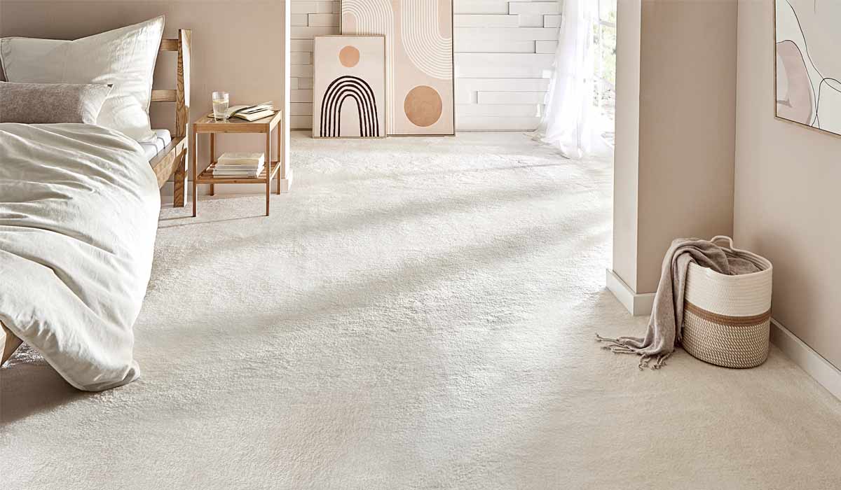 Bett steht neben Nachttisch mit Glas, helle Kunstwerke lehnen an Wand, Körbchen mit Decke im Raum