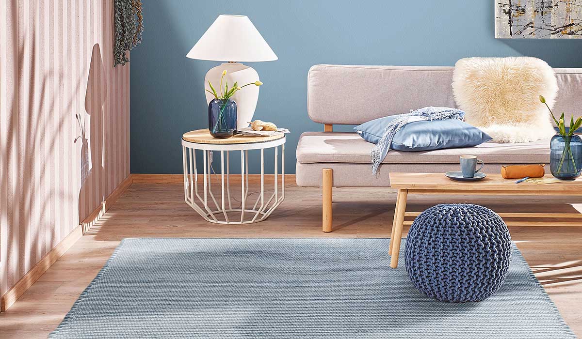 Beistelltisch mit Lampe und Vase steht vor Sofa mit Kissen und Decke, Wohnzimmer mit Teppich.