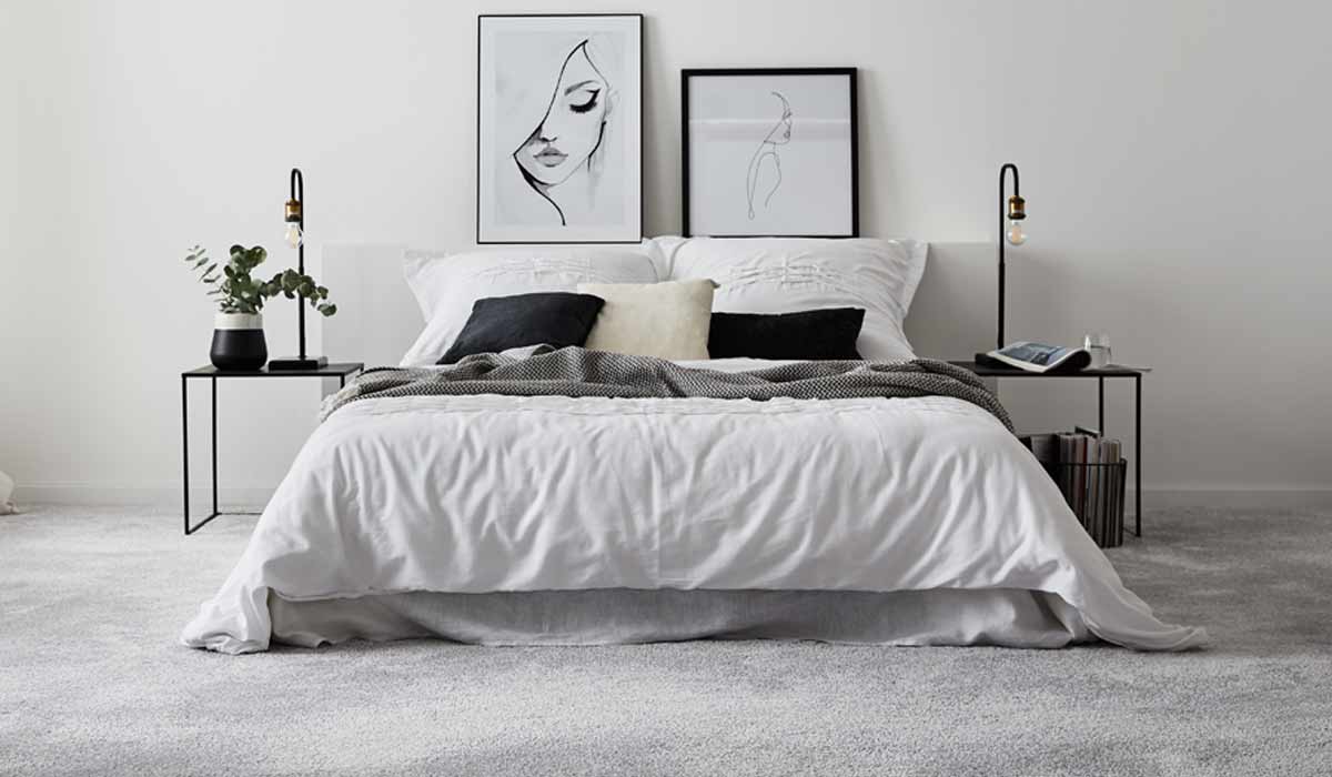 Modernes Bett mit weißen und schwarzen Kissen, zwei Nachttische mit Lampen und minimalistischen Bilderrahmen.